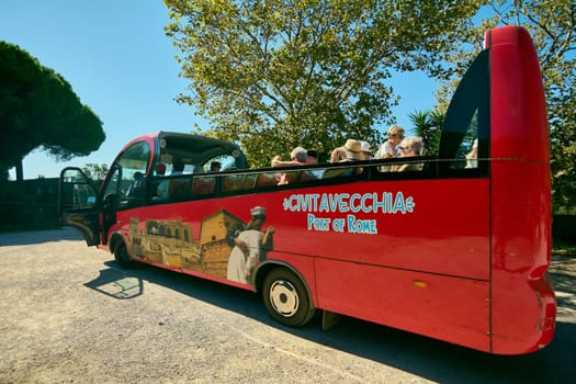 Civitavecchia. Italy - January 25, 2025: A vibrant red tourist bus with passengers, parked under a clear blue sky in Civitavecchia, Italy. The bus features images of local landmarks and the text Civitavecchia Port of Rome