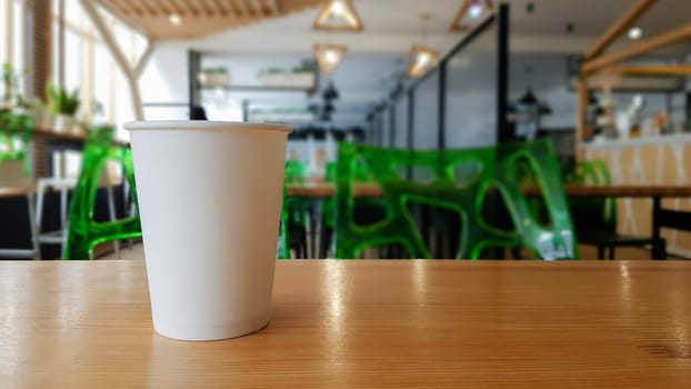Paper white coffee cup disposable to take or go, on the wooden table of the coffee shop or dining room, place for a designer layout. Hot coffee cup in a cafe