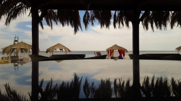 Round glass table, which depicts palm trees, sea and sky. Beautiful view of the beach in a tourist town. Summer bar on the Red Sea. Pergolas with sun loungers to protect from the sun