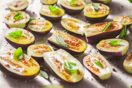 Small raw eggplants prepared for baking on baking sheet with herbs and spices