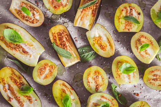 Small raw eggplants prepared for baking on baking sheet with herbs and spices