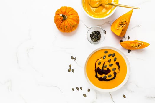 Homemade pumpkin soup with pumpkin oil and seeds on marble background
