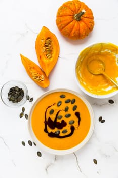 Homemade pumpkin soup with pumpkin oil and seeds on marble background