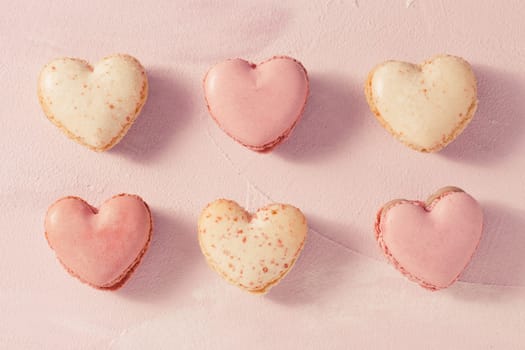 Delicious French macarons in heart shape on pink background