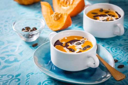 Homemade pumpkin soup with coconut milk, pumpkin oil and seeds on blue background