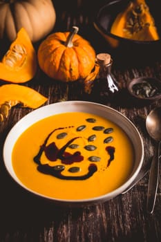 Homemade pumpkin soup with pumpkin oil and seeds on wooden background