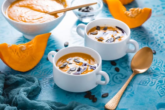 Homemade pumpkin soup with coconut milk, pumpkin oil and seeds on blue background