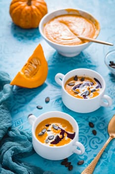 Homemade pumpkin soup with coconut milk, pumpkin oil and seeds on blue background