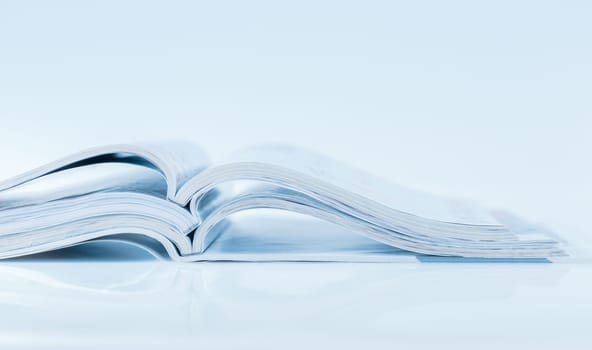 Stack of open magazines in blue tone on white background with copy space