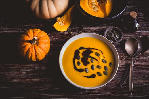 Homemade pumpkin soup with pumpkin oil and seeds on wooden background