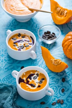 Homemade pumpkin soup with coconut milk, pumpkin oil and seeds on blue background