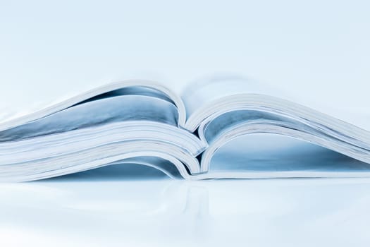 Stack of open magazines in blue tone on white background with copy space
