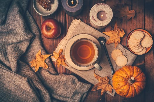 Hot tea with cookies, apple and fall foliage and pumpkins on wooden background