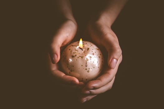 Hands holding Christmas candle on black, symbol of faith and religion