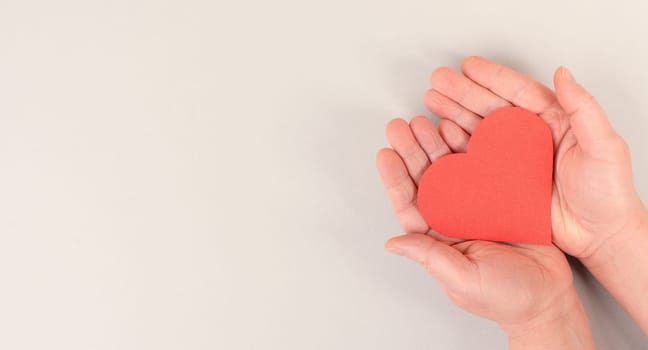 Woman is holding a red heart in her hand, world heart day, grey colored background, heartbeat, health issues