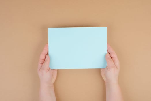 Woman holds a blank sheet of paper, brown colored background, empty copy space for text, minimalism