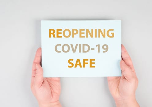 Reopening covid-19 safe, hands hold paper, message, information pandemic, grey background, sign with text