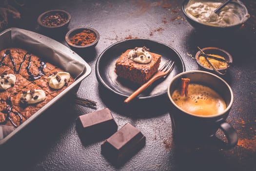 Homemade brownies with cup of coffee and baking ingredients on brown background