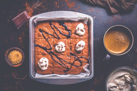 Homemade brownies with cup of coffee and baking ingredients on brown background