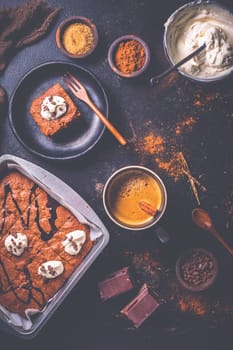 Homemade brownies with cup of coffee and baking ingredients on brown background