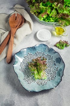 Modern ceramic bowl with wooden salad cutlery and bowl of lettuce on stone background