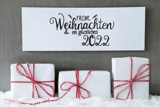 Sign With German Calligraphy Frohe Weihnachten Und Ein Glueckliches 2022 Means Merry Christmas And A Happy 2022. Three White Gifts With Red Ribbon On Snow And Cement Background