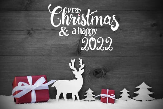 English Calligraphy Merry Christmas And A Happy 2022. Red Christmas Decoration Like Tree, Gift, And Reindeer. Black Wooden Background With Snow