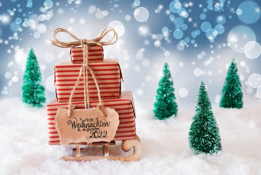 Sled With Christmas Gift And Label With German Frohe Weihnachten Und Ein Glueckliches 2022 Means Merry Christmas And A Happy 2022 Snow With Christmas Tree And Blue Sparkling Background