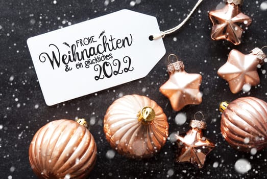 One Label With German Calligraphy Frohe Weihnachten Und Ein Glueckliches 2022 Means Merry Christmas And A Happy 2022. Golden Christmas Ball Ornament On Black Background And Snowflakes