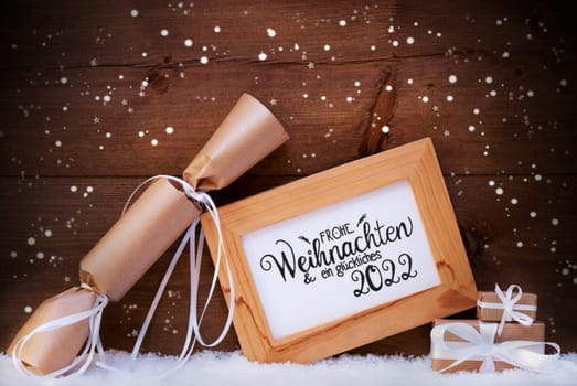 Frame With German Calligraphy Frohe Weihnachten Und Ein Glueckliches 2022 Means Merry Christmas And A Happy 2022. Christmas Decoration Like Gift And Present. Wooden Background With Snow And Snowflake