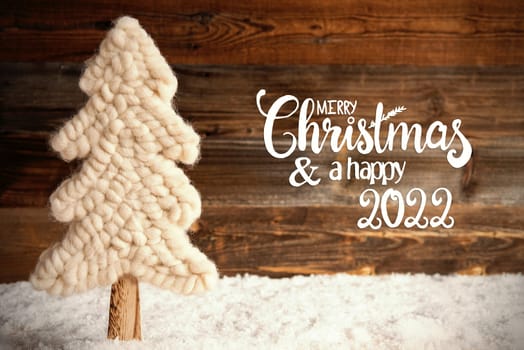 English Calligraphy Merry Christmas And A Happy 2022. White Fabric Christmas Tree With Snow. Brown Rustic Wooden Background