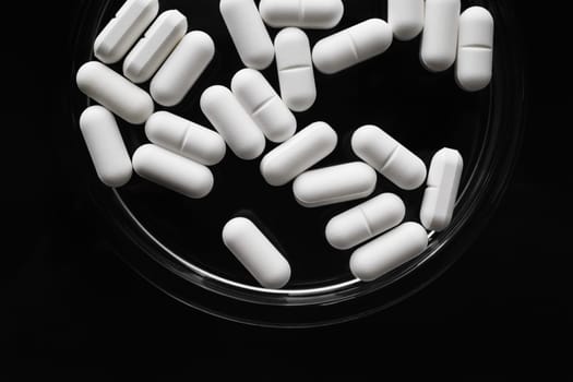 White medicine pills spilled on black background. Flat lay.