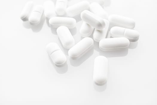 White medicine pills spilled on white background. Selective focus.