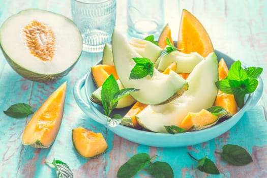 Healthy snack - Piel de sapo melon and cantaloupe with fresh mint on cyan wooden table
