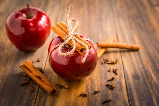 Organic red apples with cinnamon stick and cloves as baking ingredients on wooden background