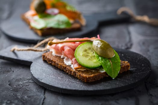 Open sandwich with prosciutto on black bread (pumpernickel) on cutting board