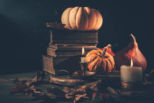 Still life for Halloween and Thanksgiving with old books, pumpkins and candle on dark background