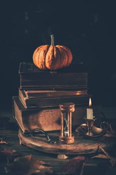 Still life for Halloween and Thanksgiving with old books, pumpkins and candle on dark background