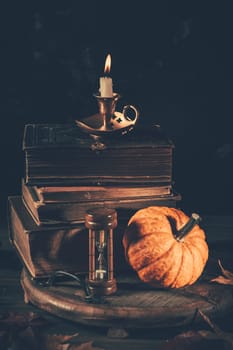 Still life for Halloween and Thanksgiving with old books, pumpkins and candle on dark background
