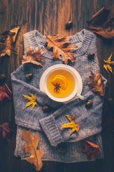 Warm sweater with hot lemon tea with fall foliage on wooden background