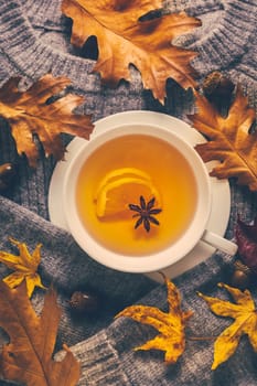 Warm sweater with hot lemon tea with fall foliage on wooden background