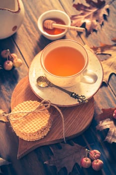 Hot tea with honey, homemade wafer biscuit and autumn leaves on wooden background