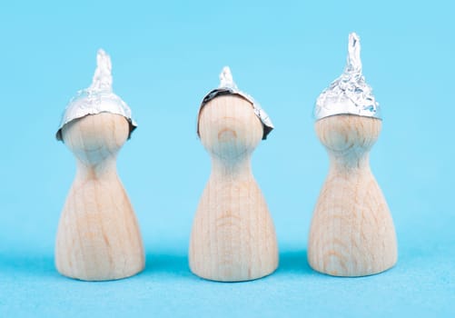 Three wooden figures wearing an alu hut, conspiracy theories, tin foil, symbolic, speech bubble, torn paper