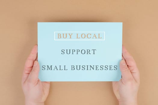 Buy local, support small businesses, enviromental shopping, text on paper, brown background, phrase, hands hold message