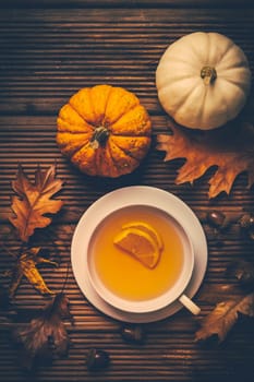 Hot lemon tea with fall foliage and pumpkins on wooden background