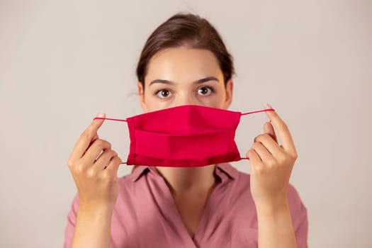 Attractive girl in pink clothing showing a protective cloth mask to the camera before putting it on. Female medical worker in studio with a flu mask in her hands.