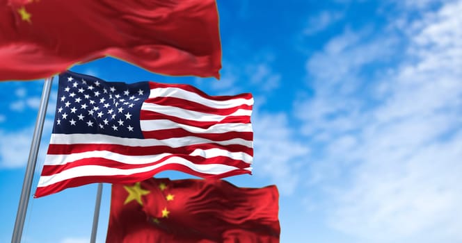The National Flag of the United States Waving Between Two Flags of China with clear sky in the background. International relations and diplomacy.