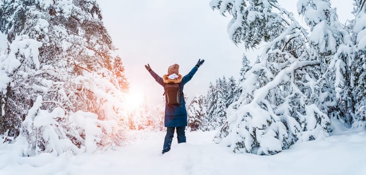 Happy woman with hands up standing in the snowy forest in snowfall. Concept of vacation and holidays.