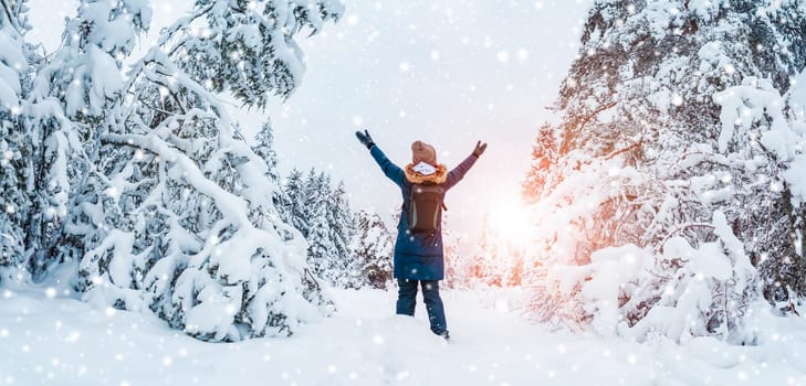 Happy woman with hands up standing in the snowy forest in snowfall. Concept of vacation and holidays.
