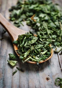 Spoon of dried green tea leaves on wooden background
